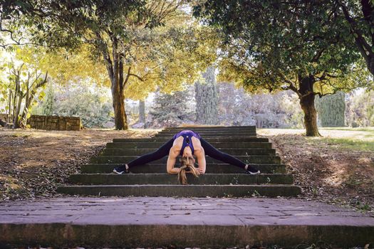 young woman runner doing some warm up exercises and stretching legs before running, sports girl at the park in morning with sunlight
