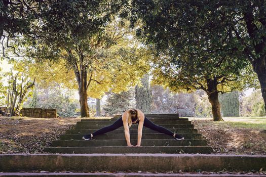 young woman runner doing some warm up exercises and stretching legs after running, sports girl at the park in morning with sunlight