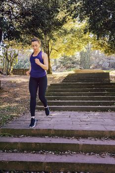 front view of young sports woman running downstairs during fitness workout at the park in the morning with sunlight, sport and healthy lifestyle concept, vertical photo