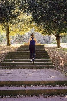 back view of young sports woman running upstairs during fitness workout at the park in the morning with sunlight, sport and healthy lifestyle concept, vertical photo