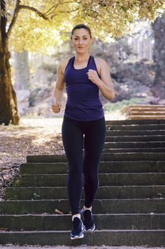 front view of young sports woman running downstairs during fitness workout at the park at the morning with sunlight, sport and healthy lifestyle concept, vertical photo