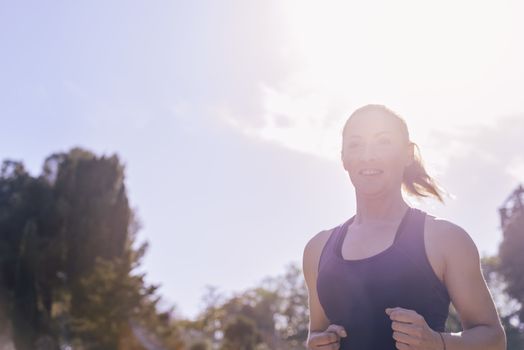 portrait of a sports woman running during outdoor workout at the park at the morning with sunlight, sport and healthy lifestyle concept