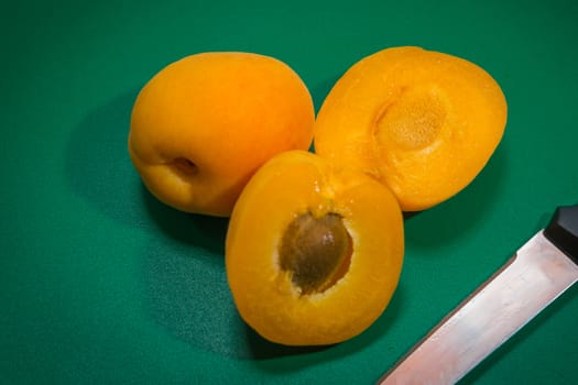 Two apricots and a knife on a green plastic, one cut in half