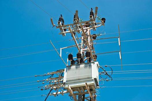 
  Power transformer for an urban area, lit by a bright sun, on a metal pole isolated against a blue sky