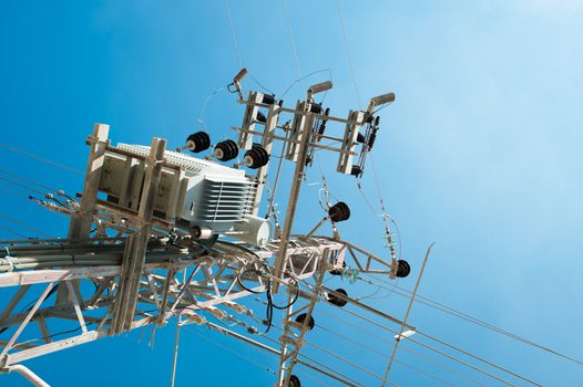 
  Power transformer for an urban area, lit by a bright sun, on a metal pole isolated against a blue sky