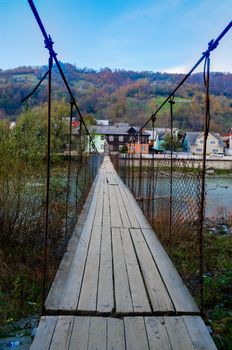 Old suspension bridge on two steel cables with wooden flooring across the river in a mountain village