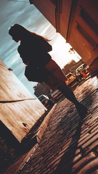 Silhouette of a girl who, in the rays of the sun, walks on a stone pavement in a European city, the concept of a happy trip, a holiday in Europe