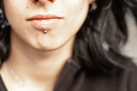 face expression from a black haired girl with metal chin piercing. black sweater on her.