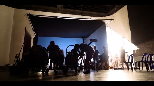 Behind the shooting of video online commercial production and film crew team working and setting light or camera or soft box and equipment set up in big studio in silhouette style