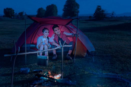 Couple of travelers spending time in tent near campfire