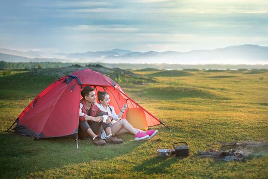 Couple of travelers spending time in tent near campfire