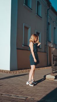 Attractive woman in dress walks through the old city streets on a sunny day. Vertical photo