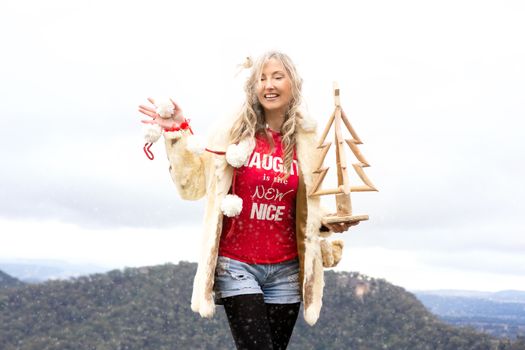 Festive woman celebrating Christmas in July or Christmas in Blue Mountains Australia.  She has a cheeky smile and is standing on a cliff with mountain backdrop.
