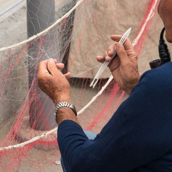 Old fisherman reparing fishing net, sitting with pipe in his mouth.