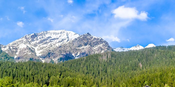 Stunning photograph of Kashmir valley (Paradise on Earth). Beautiful view of Gulmarg village surrounded by snow frozen Himalayas glacier mountains and green fir and pine tree line forest landscape.