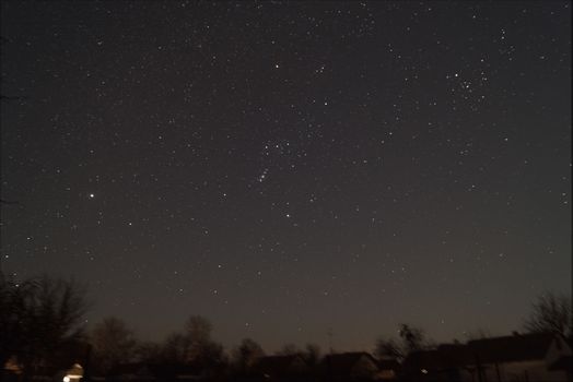 A lond exposure low light photo of village and  night sky. Village far away from city, on sky a lot of stars and constellations. Stock photo of deep sky.