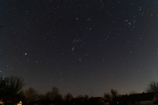 A lond exposure low light photo of village and  night sky. Village far away from city, on sky a lot of stars and constellations. Stock photo of deep sky.