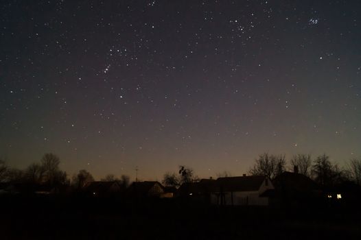 A lond exposure low light photo of village and  night sky. Village far away from city, on sky a lot of stars and constellations. Stock photo of deep sky.