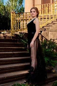 Young attractive woman in the sexy see-through, transparent, transpicuous, diaphanous black dress posing at summer sunny day outdoor at the old stairs. Fashion woman. Young woman modern portrait.