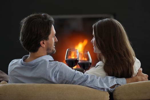 Romantic couple drinking red wine at home near fireplace