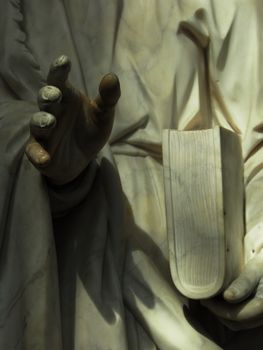 details of ancient statue, a hand and a book in low light