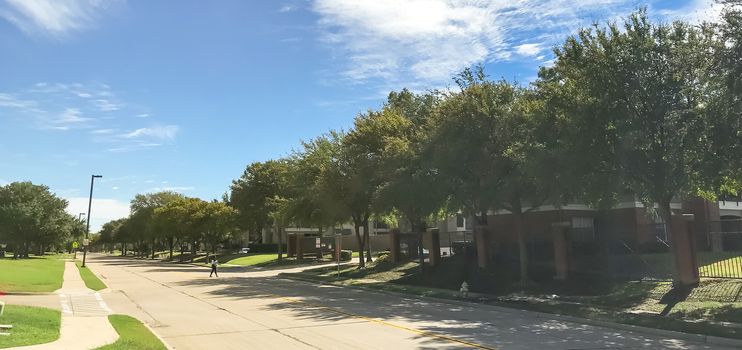 Panorama view typical three stories apartment building complex in suburban Dallas, Texas, USA. Rental living property and metal fence near street with sidewalk