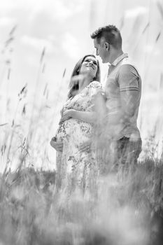 Young happy pregnant couple hugging in nature. Concept of love, relationship, care, marriage, family creation, pregnancy and parenting. Artistic black and white image.