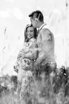 Young happy pregnant couple hugging in nature. Concept of love, relationship, care, marriage, family creation, pregnancy and parenting. Artistic black and white image.