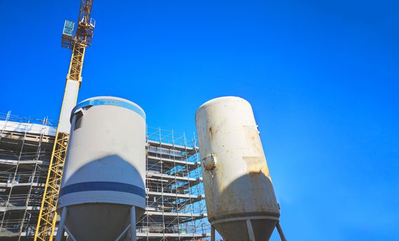 mortar silos at construction site with crane and blue sky .