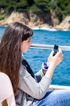 Teen girl enjoys spring vacation in a sea voyage on a pleasure boat. She sits on the upper deck communicates by video call.