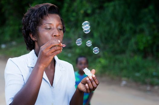 pretty young woman blowing bubbles and her child looks in the background.