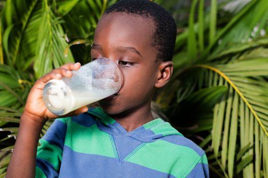 boy drinks milk behind the house near a flower.