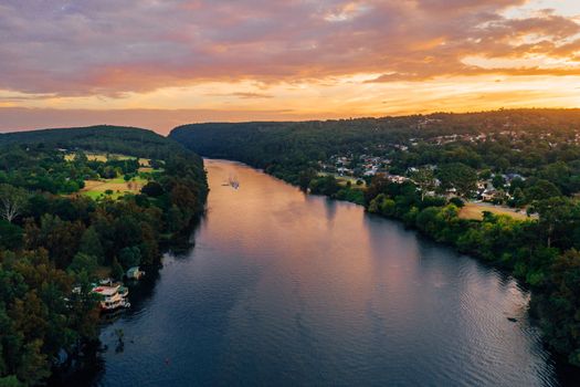 A speed boat travelling north along Nepean River as beautiful sunset colours the clouds and reflects in the water. In the foreground the Nepean Belle paddle steamer in its moorings.