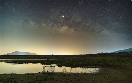 The stars in the sky reflect the light at night. The Milky Way above the mountains and the pond Mae Prachan Dam and Reservoir, Phetchaburi, Thailand