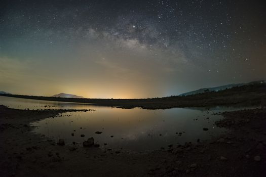 The stars in the sky reflect the light at night. The Milky Way above the mountains and the pond Mae Prachan Dam and Reservoir, Phetchaburi, Thailand