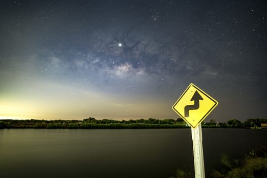 Signs, signs, beware of curves at night, behind the sign, with the Milky Way.	