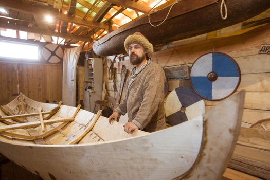 Handmade wooden boat in the barn and reenactor in medieval clothes