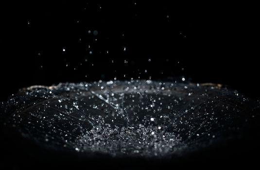 The splash of water drops in loudspeaker on black background. Perpetual motion, music and power concept.