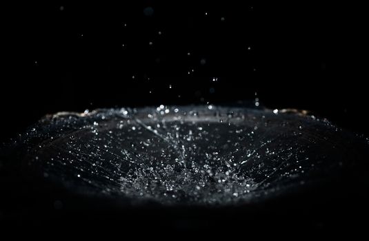 The splash of water drops in loudspeaker on black background. Perpetual motion, music and power concept.