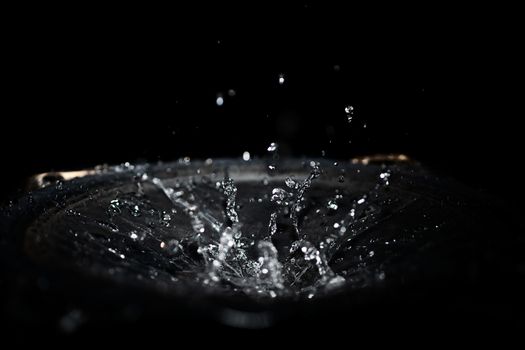 The splash of water drops in loudspeaker on black background. Perpetual motion, music and power concept.