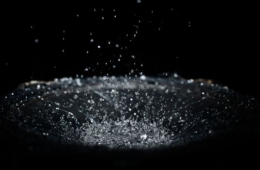 The splash of water drops in loudspeaker on black background. Perpetual motion, music and power concept.