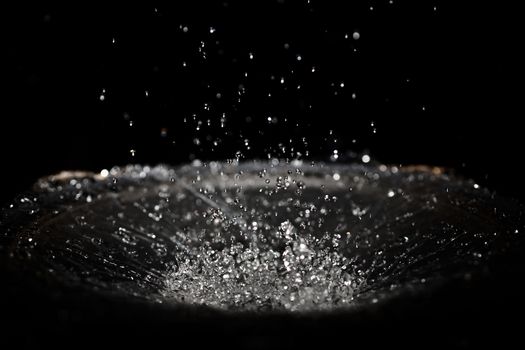 The splash of water drops in loudspeaker on black background. Perpetual motion, music and power concept.