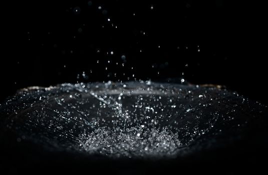 The splash of water drops in loudspeaker on black background. Perpetual motion, music and power concept.