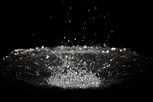 The splash of water drops in loudspeaker on black background. Perpetual motion, music and power concept.