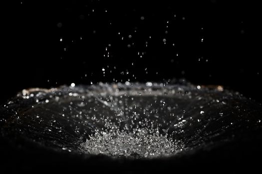 The splash of water drops in loudspeaker on black background. Perpetual motion, music and power concept.