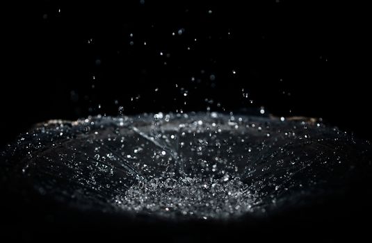 The splash of water drops in loudspeaker on black background. Perpetual motion, music and power concept.