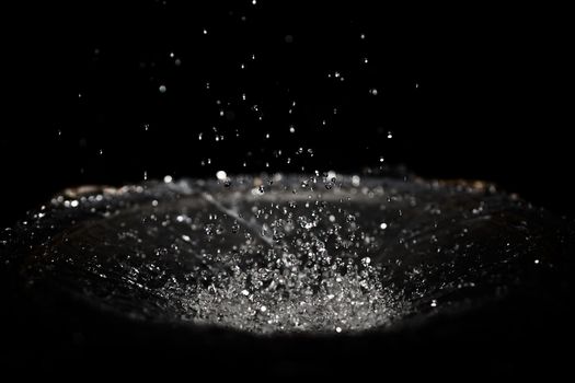 The splash of water drops in loudspeaker on black background. Perpetual motion, music and power concept.