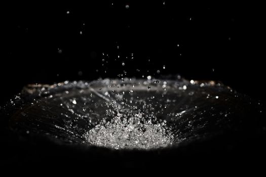 The splash of water drops in loudspeaker on black background. Perpetual motion, music and power concept.