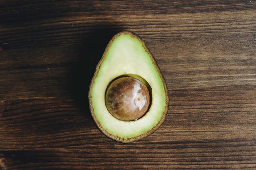 top view of half avocado with seed on wooden table, healthy vegan cuisine concept with rustic dark food photo style