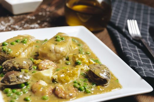 healthy traditional spanish hake dish with green seafood sauce with clams, prawns, green peas and egg, typical mediterranean cuisine with rustic dark food photo style